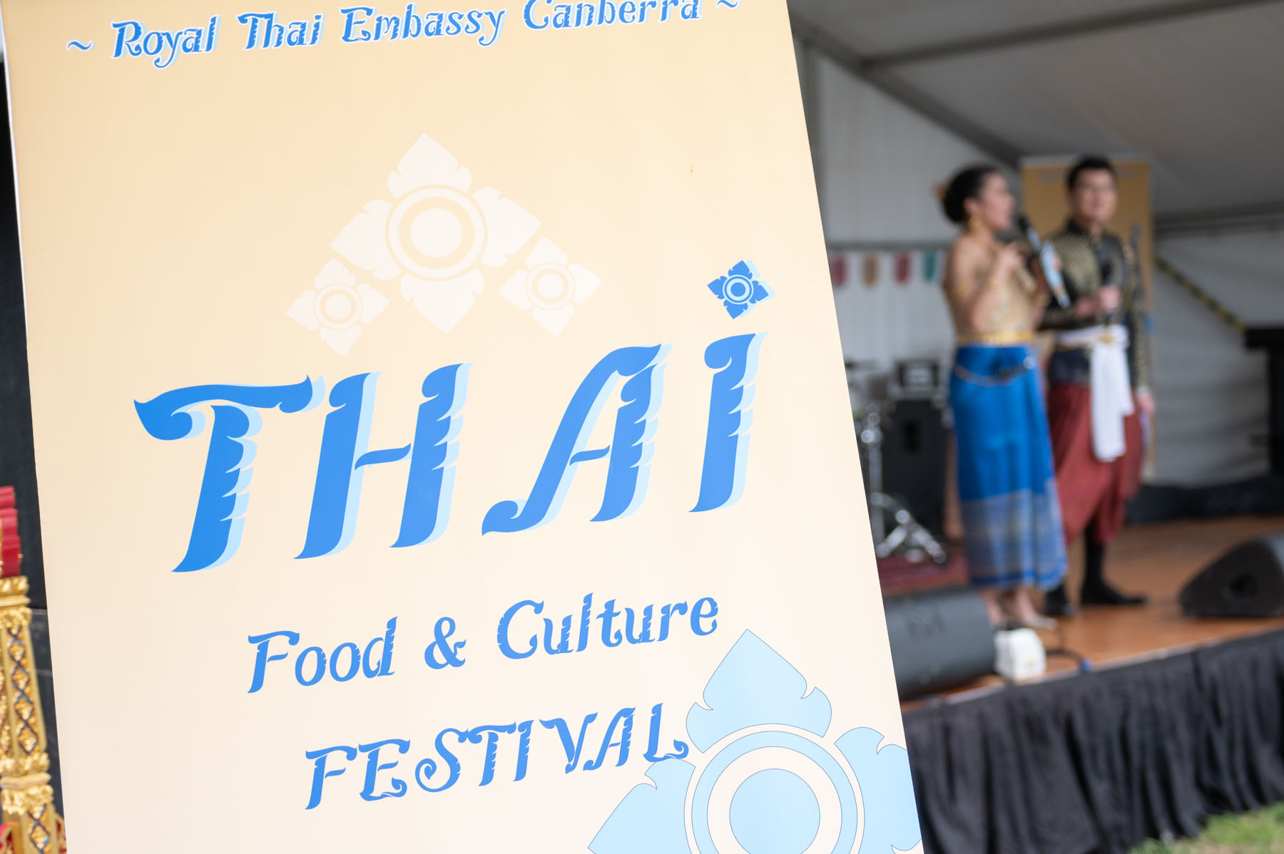 Close-up of a beige sign that reads 'Royal Thai Embassy Canberra Thai Food & Culture Festival' in blue.