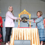 Two women simultaneously ringing a ceremonial gong, flanked by two more women in traditional Thai dress.
