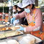 Four Thai women serve Thai food from large heated trays.