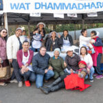 A group shot of thirteen people under a sign reading Wat Dhammadharo